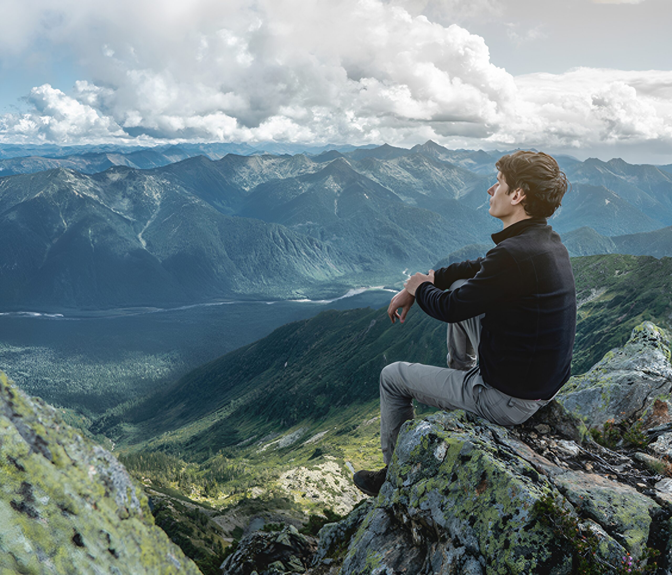 Man sitting on mountain, admiring scenic view.