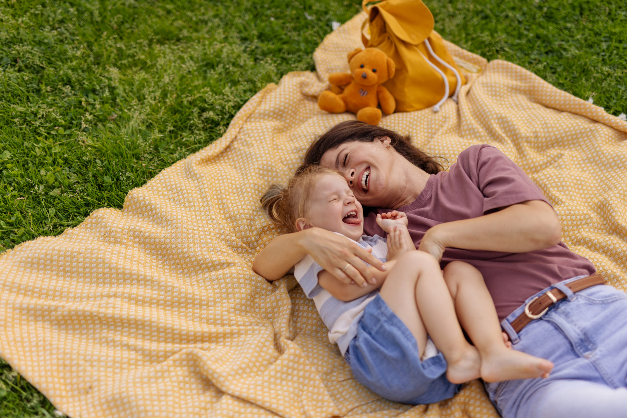 Tender family moment with a smiling mother holding her daughter close in a sunny park. Joyful parenting, connection, nature, summer vibes.