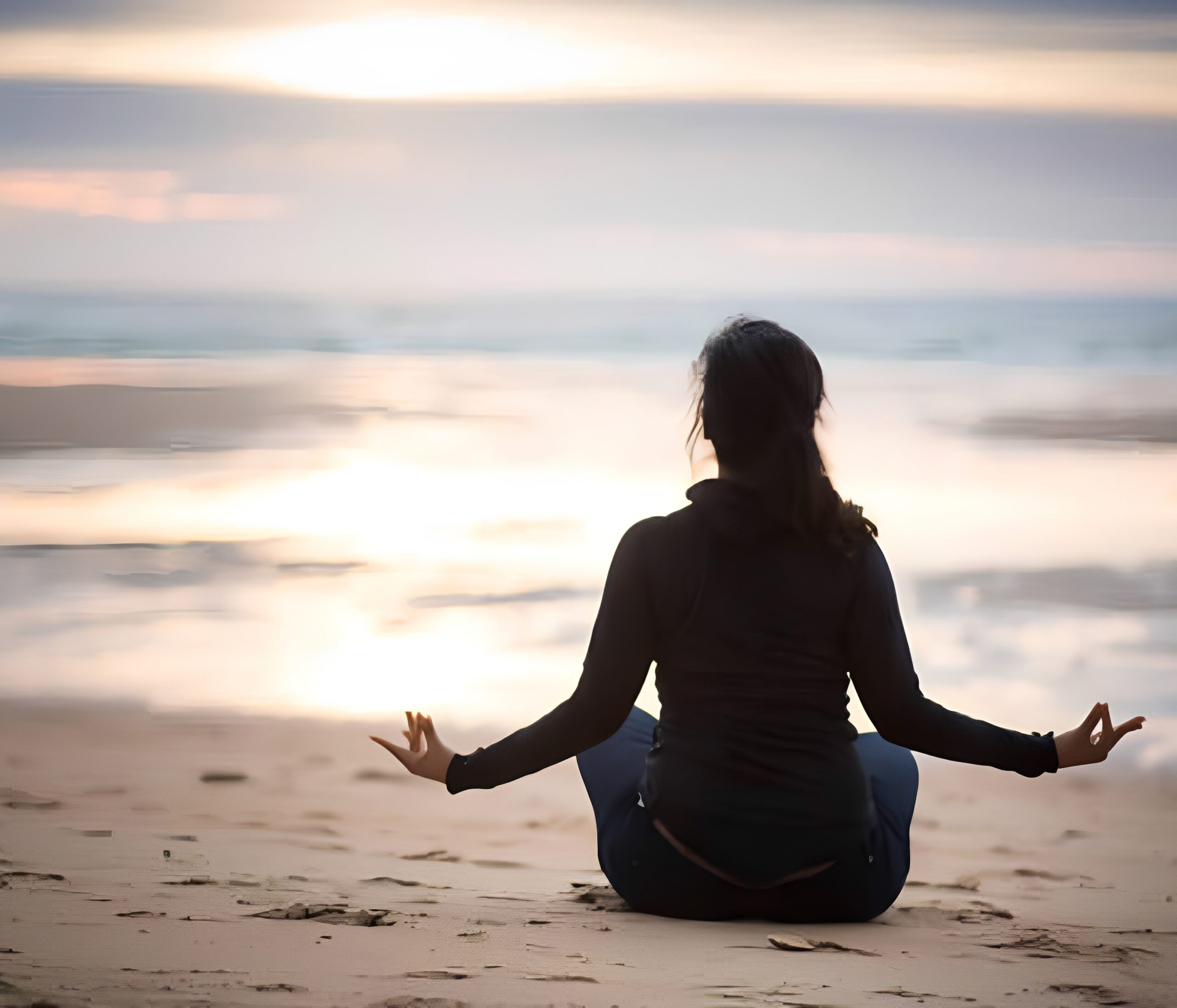 Person meditating on a beach at sunset.