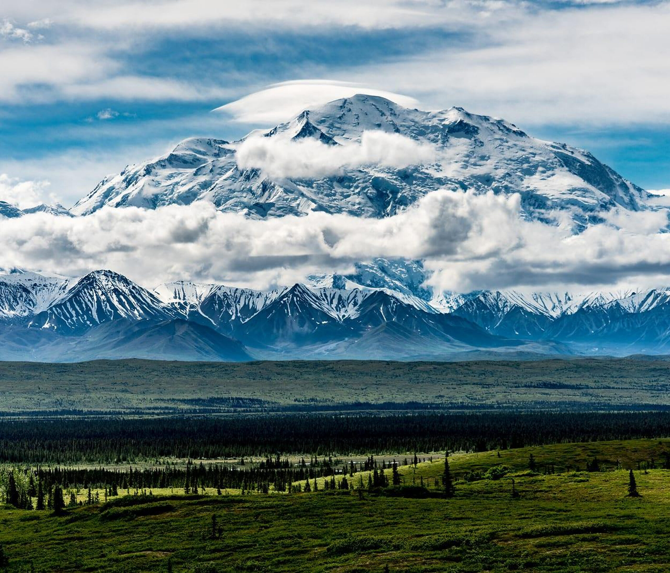Snow-capped mountain with clouds and greenery.