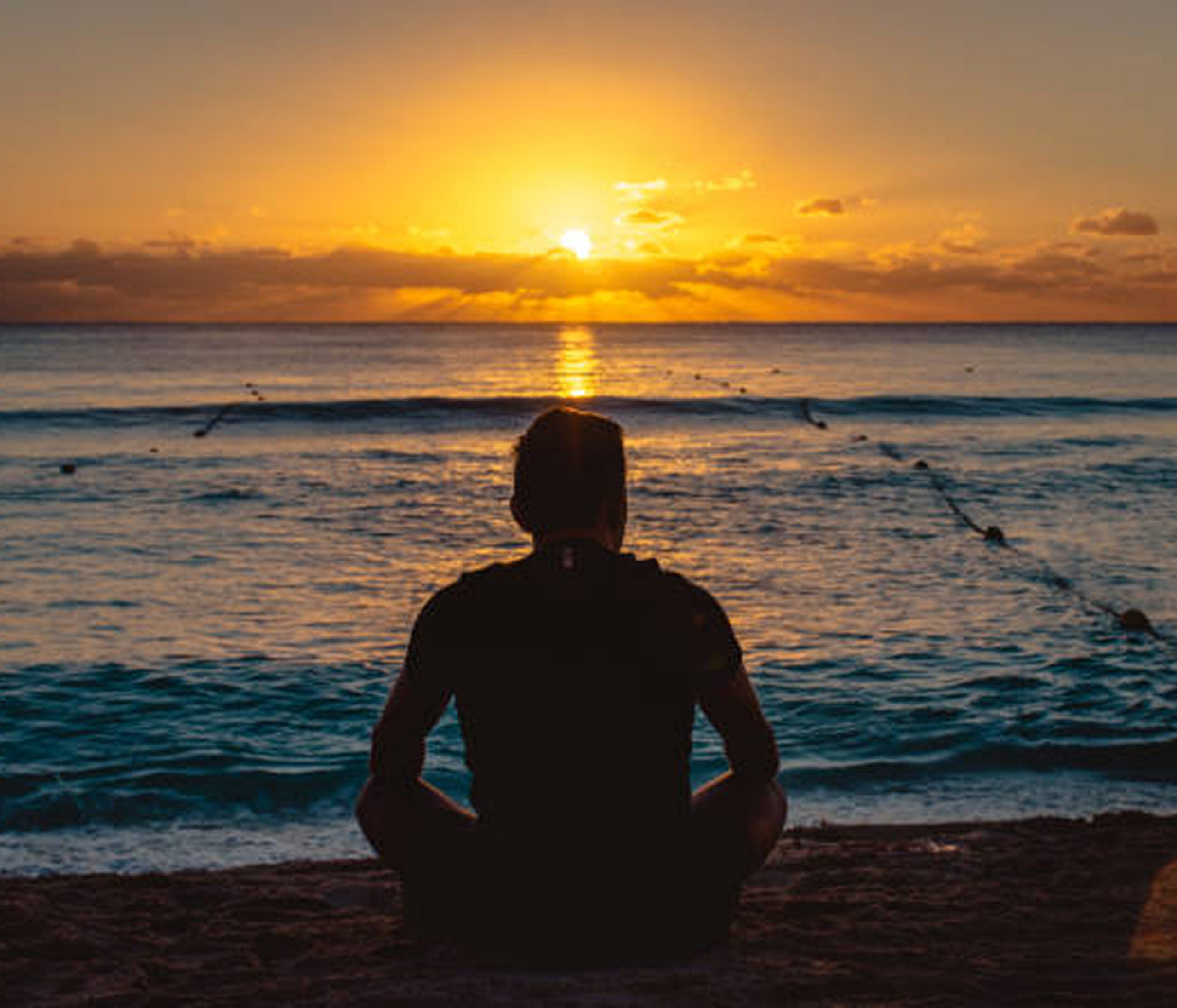Person meditating by the beach at sunset.
