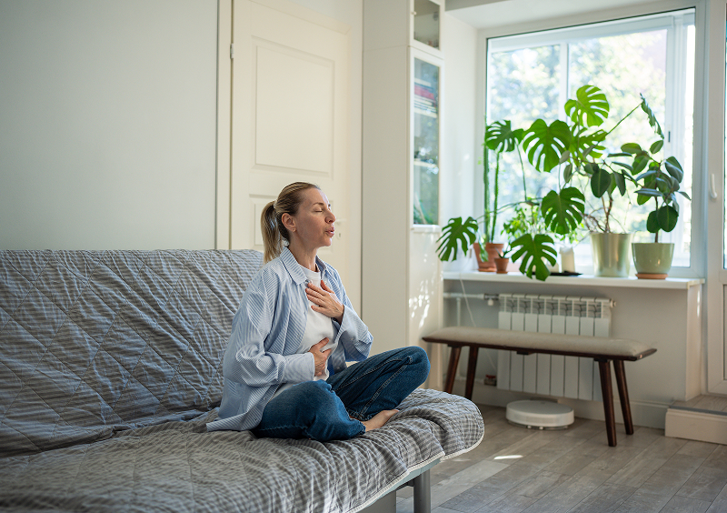 Woman meditating on a sofa, indoor plants.