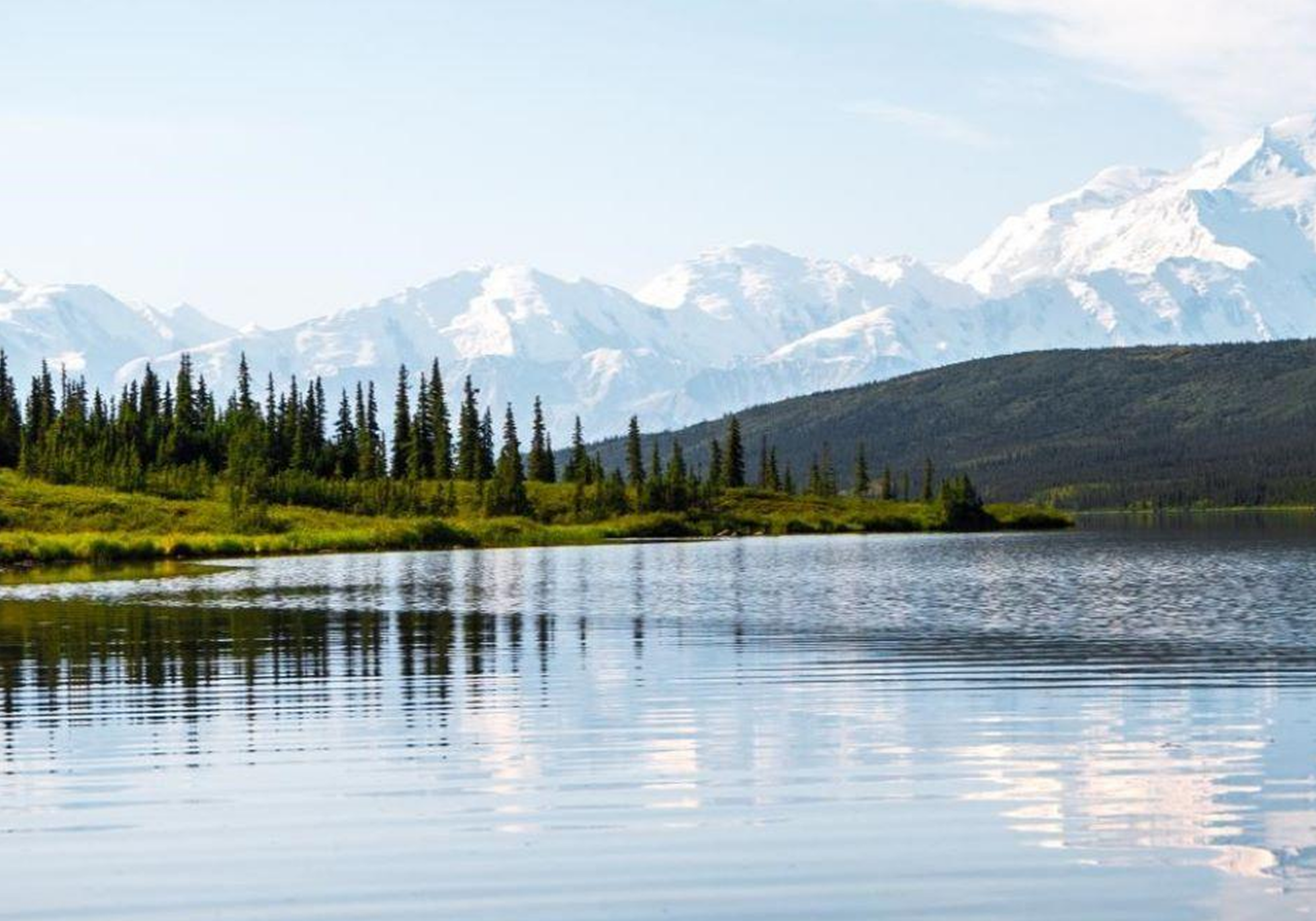 Mountain lake with forest and snowy peaks.